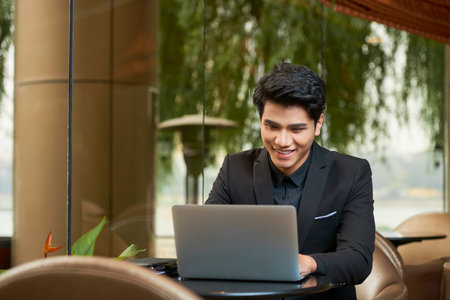 Horizontal shot of cheerful Asian young businessman working on laptop smilingの写真素材