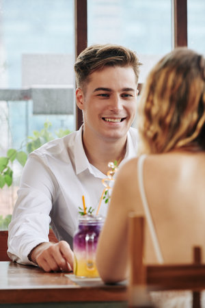 Happy Caucasian guy sitting in cafe in front of unrecognizable girl smiling, vertical portrait