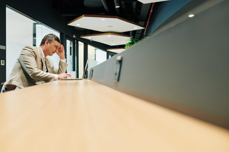 Horizontal side view long shot of middle-aged Caucasian man sitting alone in office working on laptopの写真素材