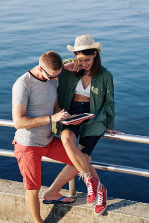 Vertical high angle shot of young man and woman watching something on their tablet PC on seafrontの写真素材