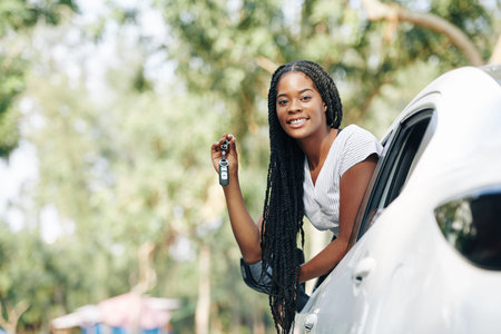 Happy young woman sticking out of car window and showing electronic car keys