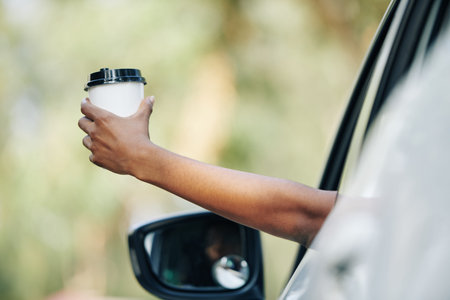 Hand of female driver holding cup of take away coffee