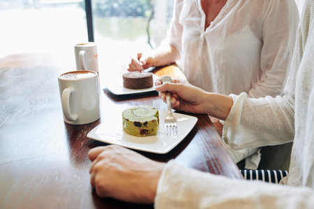 Cropped image of women enjoying delicious desserts and tasty coffee in cafe