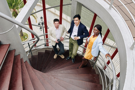 Positive young business team standing on spiral staircase and looking up at camera