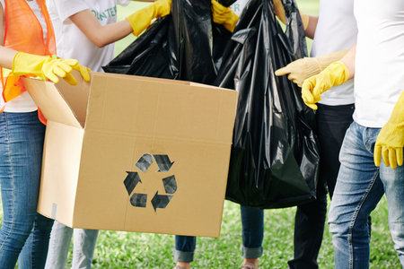 Volunteers sorting trash they collected in park and filling cardboard box for recycling and plastic...
