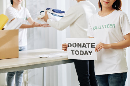 Smiling young female volunteer showing card with donate today inscription