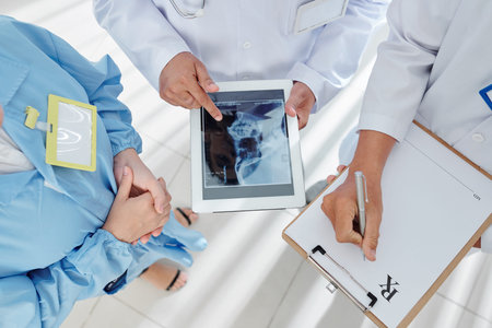 Group of physicians discussing scull x-ray on tablet computer and taking notes in prescription...