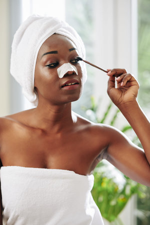 Vertical medium portrait of young African American woman applying mascara on her eyelashes