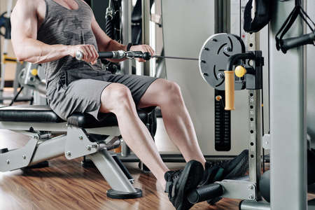 Cropped image of fit man training hard and pulling weights in seated cable row machineの写真素材