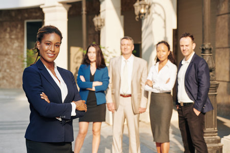Portrait of pretty successful business lady with arms folded standing in front of her business team