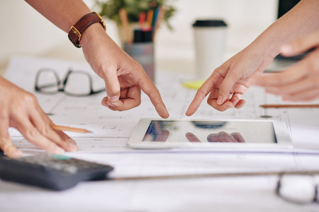 Hands of arhitect and construction engineer pointing at building plan on screen of tablet computerの写真素材