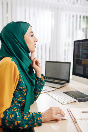 Excited female programmer sitting at office desk and writing code for mobile application