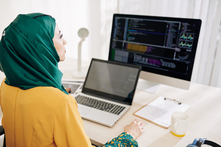 Serious female software engineer working on computer and laptop in her office