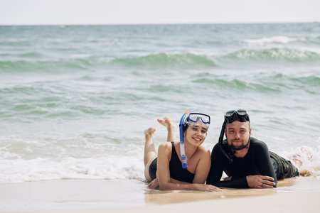 Beautiful smilng boyfriend and girlfriend resting on beach after snorkeling in seaの写真素材