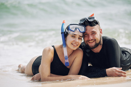 Portrait of beautiful young couple in snorkeling masks resting after diving in sea togetherの写真素材