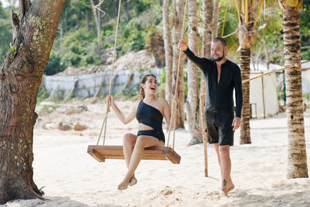 Happy young couple in love swaying on tree swing on beautiful beach and enjoying honeymoon vacationの写真素材