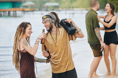 Cheerful young couple listening to music on the speaker and drinking bottled beerの写真素材