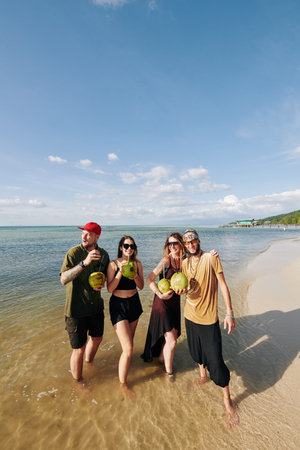 Group of happy friends drinking coconut cocktails when walking on beach of tropical island