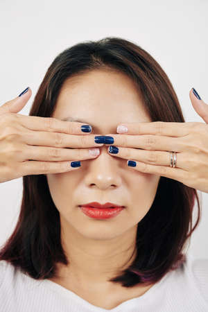 Young woman covering eyes with hands with simple dark blue manicureの写真素材