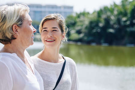 Laughing young woman listening to funny story of her mature mother when they are walking outdoorsの写真素材