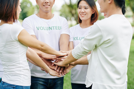 Group of volunteers stacking hands before enthusiastically engage in cleaning activity in local parkの写真素材