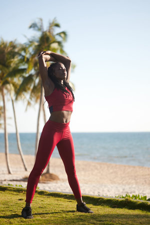 Beautiful young Black woman stretching back after running on the beach in the morning
