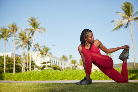 Pretty young Black flexible sportwoman stretching legs after jogging in parkの写真素材