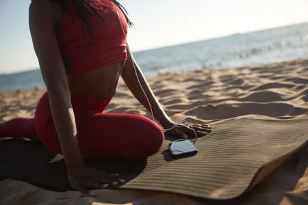Woman listening to calm music via smartphone application when sitting in pidgeon pose on yoga mat on the beachの写真素材