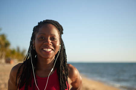 Happy young smiling woman listening to music in earbuds when spending time on the beachの写真素材
