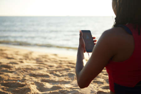 Smartphone with yoga application in hand of fit woman standing on sandy beachの写真素材