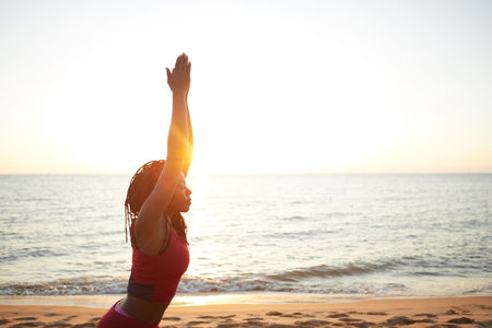 Fit young woman standing in morning sun rays and practicing warrior pose
