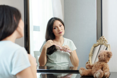 Beautiful young Asian woman sitting in front of vanity in her room and brushing hairの写真素材