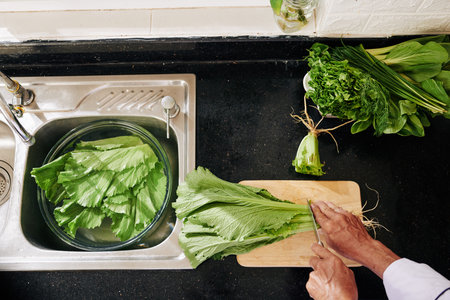 Man cutting lettuce and putting leaves in big bowl with fresh water in kitchen sink