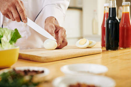 Hands of chef cutting boiled chicken eggs when cooking salad at kitchenの写真素材