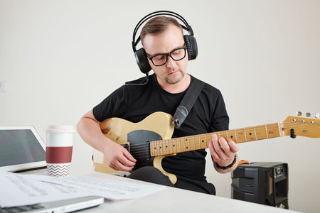 Man in glasses playing guitar when composing new song for his band