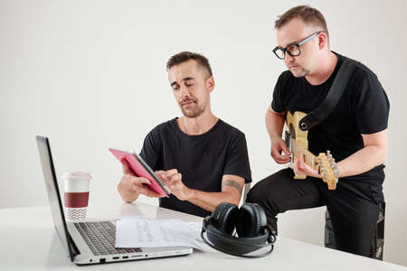 Musician following notes on tablet computer of his colleague when they are working on song for the projectの写真素材
