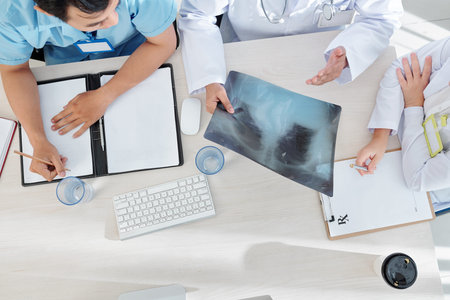 General practitioner and his interns discussing lungs x-ray of patient, writing down symptoms and...