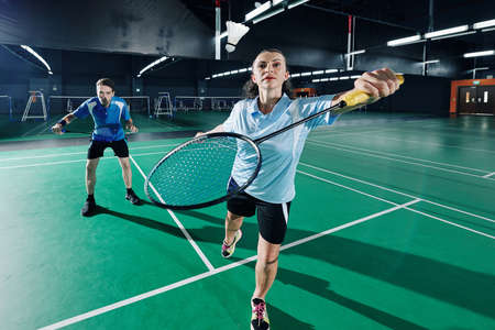Concentrated couple playing badminton in team in gymnasiumの写真素材