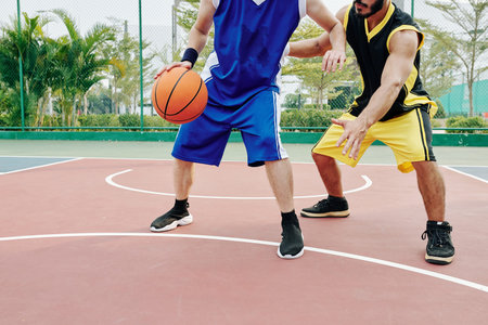 Cropped image of young men playing basketball on outdoor courtの写真素材