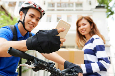 Courier checking next address via mobile application after delivering package to young womanの写真素材