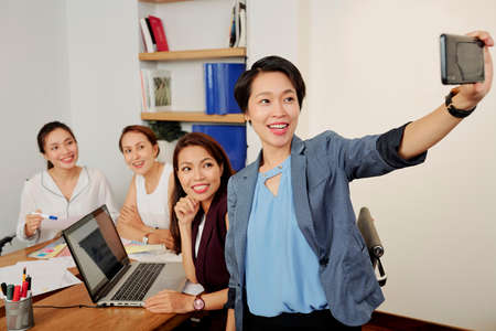 Happy young pretty business lady taking selfie with her colleagues at meetingの写真素材