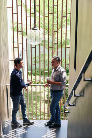 Businessmen standing on staircase, drinking take out coffee and discussing news and gossipsの写真素材