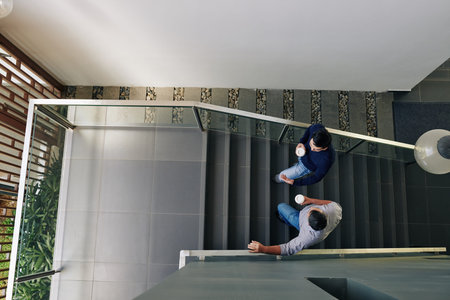 Colleagues walking up the stairs, drinking take away coffee and discussing work, view from above