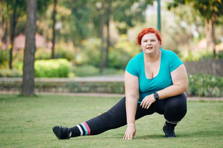 Overweight young woman stretching legs and warming up before training in parkの写真素材