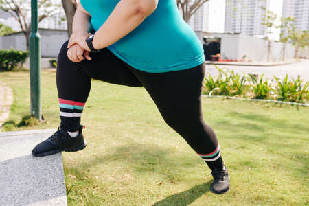 Cropped image of young overweight woman putting leg on parapet and stretching it after joggingの写真素材