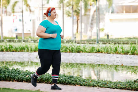 Overweight woman enjoying running in park and listening to music in headphonesの写真素材