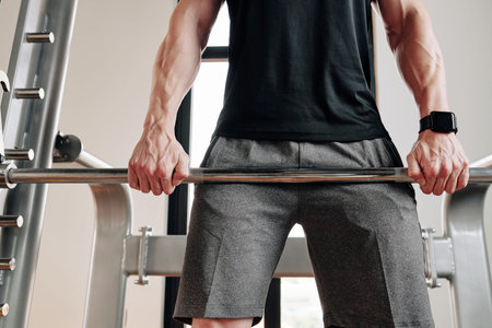 Cropped image of strong fit man lifting barbell in gym and doing Romanian deadlift