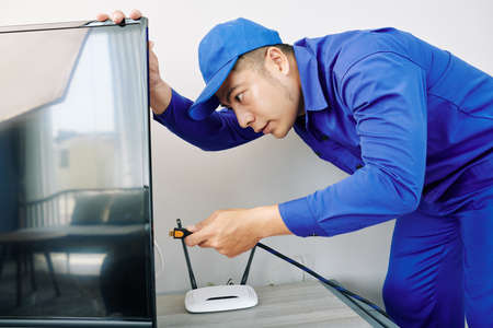 Electrician inserting plug in tv screen when installing devices in living room of clientの写真素材