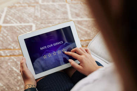 Woman rating service and leaving feedback via application on tablet computerの写真素材