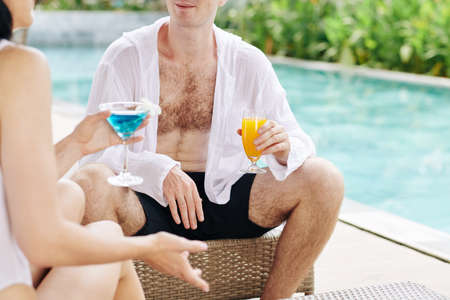 Young couple spending time by swimming pool, drinking delicious cocktails and discussing newsの写真素材